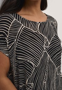 Haut noir avec des motifs de lignes abstraites blanches contrastantes, col rond, manches courtes et tissu texturé.