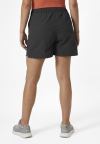 Černé šortky vyrobené z lehkého materiálu, s elastickým pasem, bočními kapsami a hladkým povrchem. Spárované se šedými teniskami.