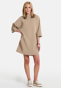 Beige, lyhythihainen mekko, jossa on korkea kaula-aukko ja löysä leikkaus, valmistettu sileästä kankaasta. Yhdistetty vaaleansävyisiin tennareihin.