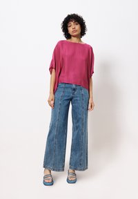 Roze, losvallende, kortmouwige top met een gladde textuur, gecombineerd met wijde, hooggewicht blauwe spijkerbroeken met een verticale naad.