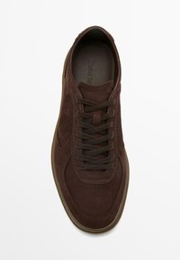 Mörkbrun sneaker i mocka med matchande snören, perforerad tåventilation och sula i gummigummi, sedd ovanifrån mot en vit bakgrund.