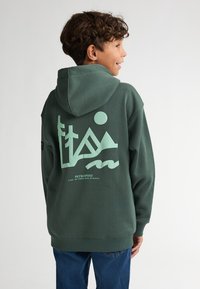 Groene hoodie van katoen met een grote lichtgroene afbeelding van bergen en golven op de achterkant, voorzien van een capuchon met trekkoord en geribbelde manchetten.
