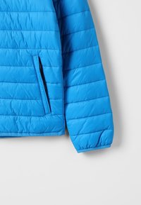 Polstrovaná modrá bunda s horizontálním prošíváním, postranní kapsou na zip a elastickými manžetami. Hladká, voděodolná látka.