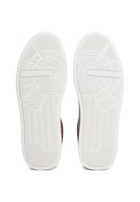 Weiße Gummisohlen eines Paar Sneakers mit kreisförmigen und Zickzack-Laufsohlenmustern sowie dem „Tommy Hilfiger“-Logo in der Mitte.