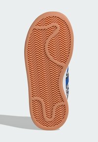 Shoe sole featuring a textured wave pattern in orange rubber, outlined by a white edge and accentuated with blue and patterned side details.