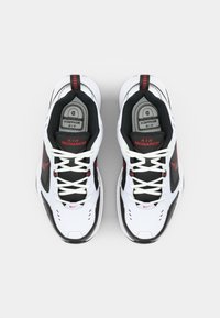 Pantofi sport albi cu accente negre și detalii roșii. Prezintă un design din plasă, o talpă căptușită și un sistem de șireturi tradițional.