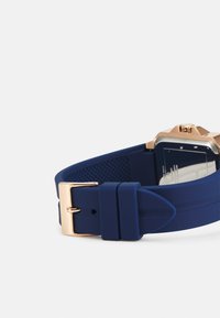 Blaue Silikon-Uhrenarmband mit einer goldfarbigen Metallschnalle. Verfügt über eine strukturierte Oberfläche und mehrere verstellbare Löcher zur Größenanpassung.