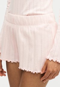 Gros plan d'une personne portant un short côtelé rose doux avec un ourlet à volants et un haut assorti à manches longues.