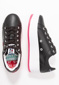 Černé kožené tenisky s bílou podrážkou a růžovými akcenty. Mezi rysy patří kulaté tkaničky, šité detaily a logo na jazyku.