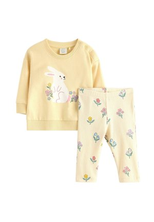 Completo giallo per bambino piccolo con maglietta a maniche lunghe che presenta un coniglio bianco e una stampa floreale, abbinato a leggings a coste con fiori colorati.