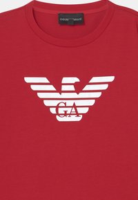 Red crewneck t-shirt with a large white Emporio Armani eagle logo and "GA" letters printed on the chest.