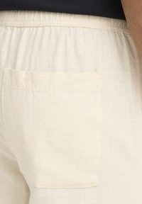 Shorts beige clair en tissu texturé, avec des rayures horizontales et une poche arrière cousue. Taille élastique pour le confort.