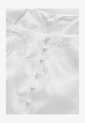 Vit linneblus med rynkad detalj runt halsringningen, med en rad av sex texturerade, runda knappar fram.