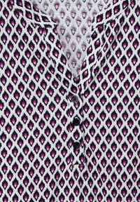 Blusa con colletto e chiusura a bottoni, caratterizzata da un motivo a diamante in bianco, nero e rosa. Tessuto morbido con una finitura testurizzata.
