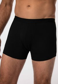 Boxer da uomo in cotone nero con una cintura morbida che presenta un logo discreto. Il tessuto è liscio con una vestibilità aderente e una copertura a metà coscia.