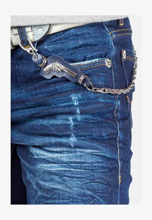 Blue denim jeans with a textured finish feature a decorative metal chain and a faux pistol keychain attached to the belt loop.