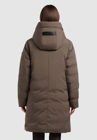 Hnědý prošívaný kabát s velkou kapucí, zipovými detaily a plochou nášivkou na zadní straně. Materiál má hladkou, matnou texturu.