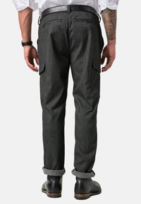 Dunkelgraue Cargo-Hosen aus strukturiertem Material, mit seitlichen Taschen und hochgerollten Säumen, kombiniert mit schwarzen Lederschuhen.