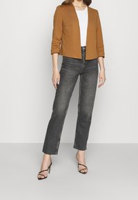 Brązowa krótka marynarka z rękawami do łokcia, zestawiona z ciemnoszarymi, wysokim stanem jeansami oraz czarnymi sandałkami na paski. Pod spodem biała koszulka.