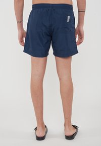 Navyblauwe zwembroek met een elastische tailleband, achterzak en logo-label. Het materiaal lijkt lichtgewicht en waterafstotend te zijn.