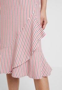 Růžová a bílá pruhovaná sukně s volánkovým lemem. Vyrobena z měkké tkaniny, s diagonálním střihem a mírně rozšířeným tvarem.