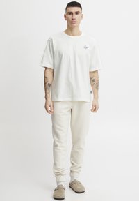 Witte katoenen T-shirt met ronde hals en korte mouwen, gecombineerd met beige sweatpants met elastische manchetten en zijzakken.