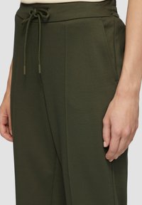 Olijfgroene high-waisted broek met zijzakken, elastische tailleband en verstelbaar trekkoord. Soepele textuur met een subtiel patroon.