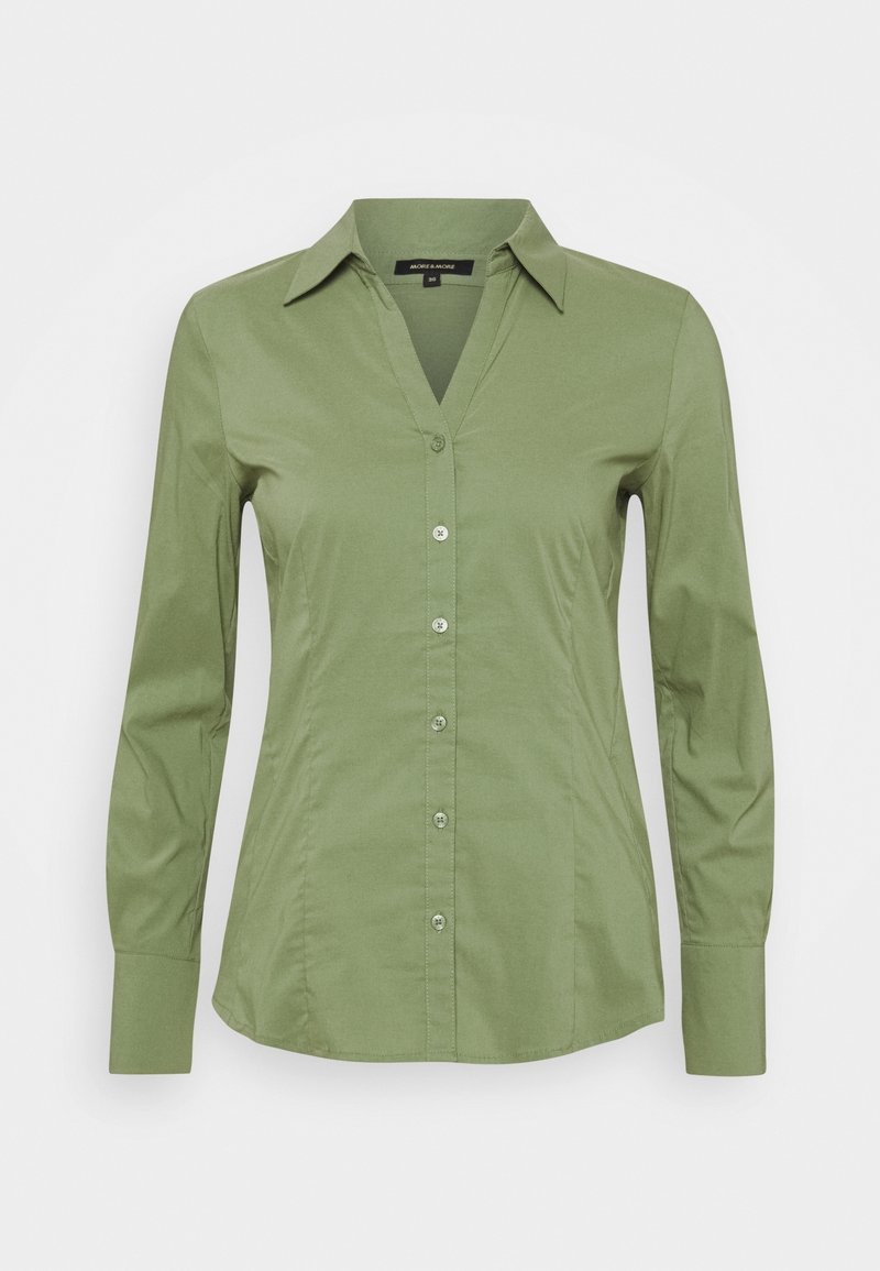 Chemise vert olive à manches longues, boutonnée, avec col pointu et coupe ajustée, présentée sur fond gris.