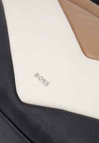 Läderväska med en tre-färgad design i svart, vitt och beige. Noterbar silverfärgad "BOSS"-logotyp i det nedre hörnet. Strukturerad yta.