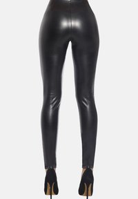 Czarne skórzane legginsy o wysokim stanie, błyszczącej fakturze i slim fit. Zestawione z czarnymi szpilkami.