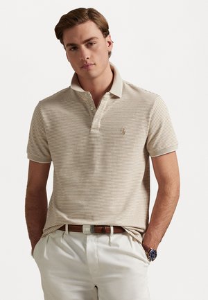 Gestreepte polo in beige en crème, korte mouwen, placket met twee knopen, geborduurd logo op de borst, gecombineerd met een bruine riem en lichte broek.