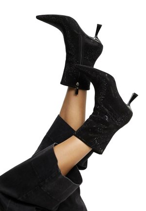 Crne gležnjače s oštrim vrhom, izrađene od teksturirane tkanine, s patent zatvaračem i uskim, visokim stiletto potplatom.
