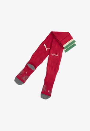 Calzettoni sportivi rossi con talloni e punte grigie, polsini a righe verdi e bianche, logo Puma e scritta araba sulla zona dello stinco.