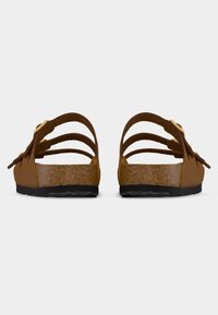 Ζευγάρι καφέ πλατφόρμες από φελλό με τρεις ρυθμιζόμενους ιμάντες και μαύρες ελαστικές σόλες, ορατές από πίσω.