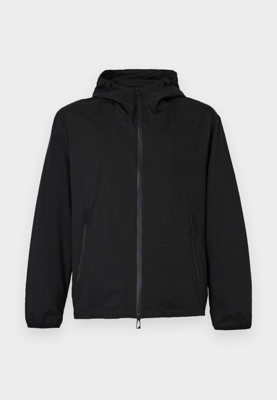 Fekete, könnyű, kapucnis dzseki elülső cipzárral és cipzáras oldalzsebekkel, elasztikus mandzsettákkal és állítható zsinórokkal a kapucnin.