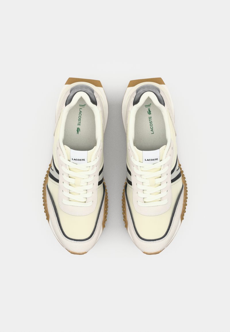 Baskets Lacoste en crème avec un design à rayures noires, dotées d'une semelle en caoutchouc texturée et d'un système de laçage. Matériau doux et intérieur rembourré.