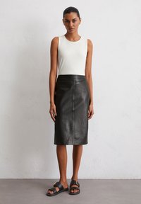 Weißes ärmelloses Top kombiniert mit einem knielangen schwarzen Lederrock. Das Model trägt schwarze Sandalen mit einer Schnalle. Glatte Texturen, einfaches Design.