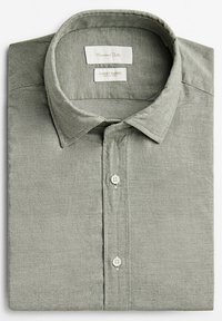 Chemise à manches longues vert clair pliée avec col, boutons sur le devant et étiquettes en tissu à l'intérieur du col.
