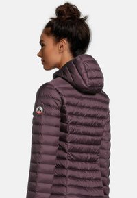 Opblaasjack in donkerpaars, met horizontale gestikte secties, een capuchon en een logopatch op de linker mouw.