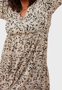 Krémové šaty s květinovým potiskem a černými akcenty. Mají výstřih do V, krátké rukávy a nařasený pas, vyrobené z lehkého materiálu.