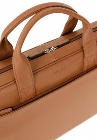 Tan leren tas met dubbele handvaten, ritscompartimenten en een zachte textuur. Kenmerken zijn ingegoten branding en zichtbare stikdetails.