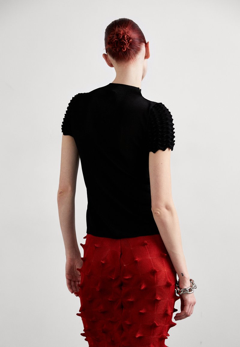 Top negro de manga corta con hombros texturizados y con volantes, combinado con una falda roja que presenta un patrón tridimensional y saliente.