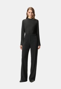 Top nero a maniche lunghe abbinato a pantaloni neri a vita alta, a gamba larga. Tessuto liscio con silhouette elegante e dettagli minimalisti.
