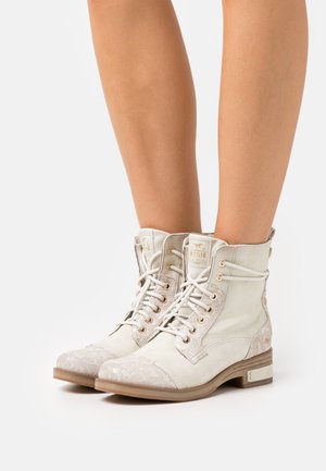 Beige ankle boots made of suede with a patterned toe cap. Features include lace-up design, gold-tone eyelets, and a low heel.