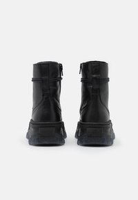 Paire de bottines en cuir noir avec semelles épaisses à rainures, fermeture éclair arrière et détail en boucle, vues de dos sur fond blanc.