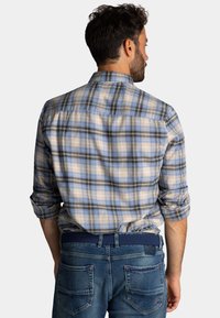 Geruite shirt in lichtblauw, beige, en zwart, met een button-down kraag en opgerolde mouwen. G gedragen met blauwe spijkerbroeken.