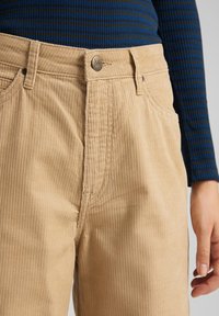 Beiga kordflöjtsbyxor med synliga vertikala ränder, utrustade med metallknäppning, fickor och subtila sömnadsdetaljer.