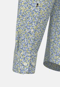 Langarmhemd met een lichtblauw, geel en wit bloemenpatroon. Bevat witte knopen en een kleine zwarte borduursel op de mouw.