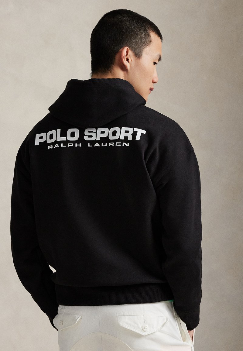 Juodas gobtuvu džemperis, pagamintas iš minkštos medžiagos, su dideliu baltu "POLO SPORT" logotipu ir "RALPH LAUREN" užrašu per nugarą.