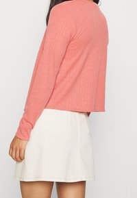 Kobaltová směs bavlny, dlouhý rukáv, top v korálové barvě s žebrovanou strukturou, zkrácený střih, kulatý výstřih, spárovaný s béžovou mini sukní.